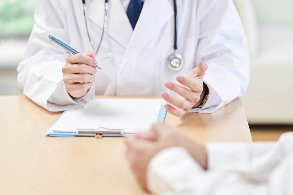 患者に対して症状を説明する医師の手のイメージ